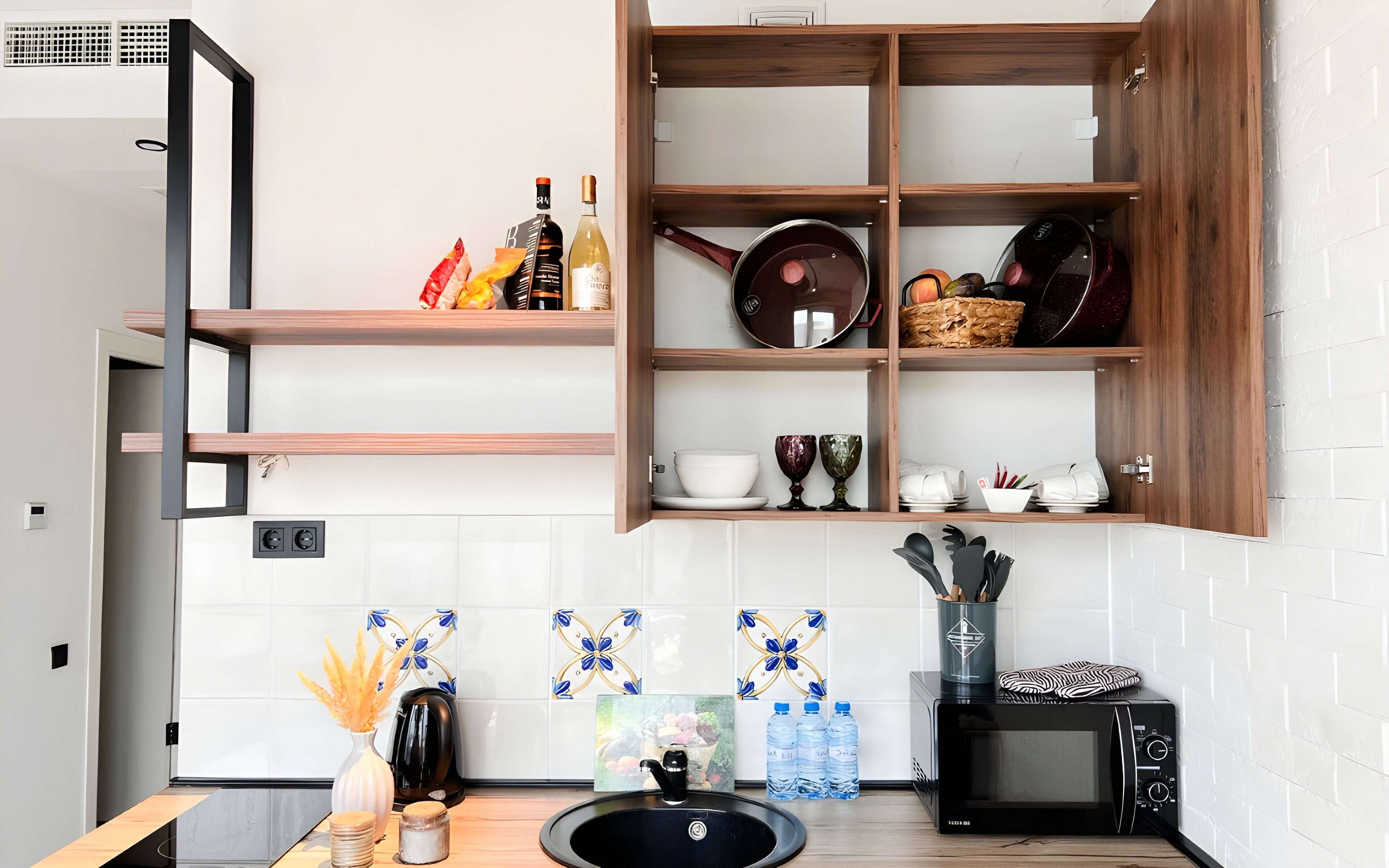 Una cocina con un armario de madera, un lavamanos, un hervidor, un microondas y un salpicadero de azulejos.