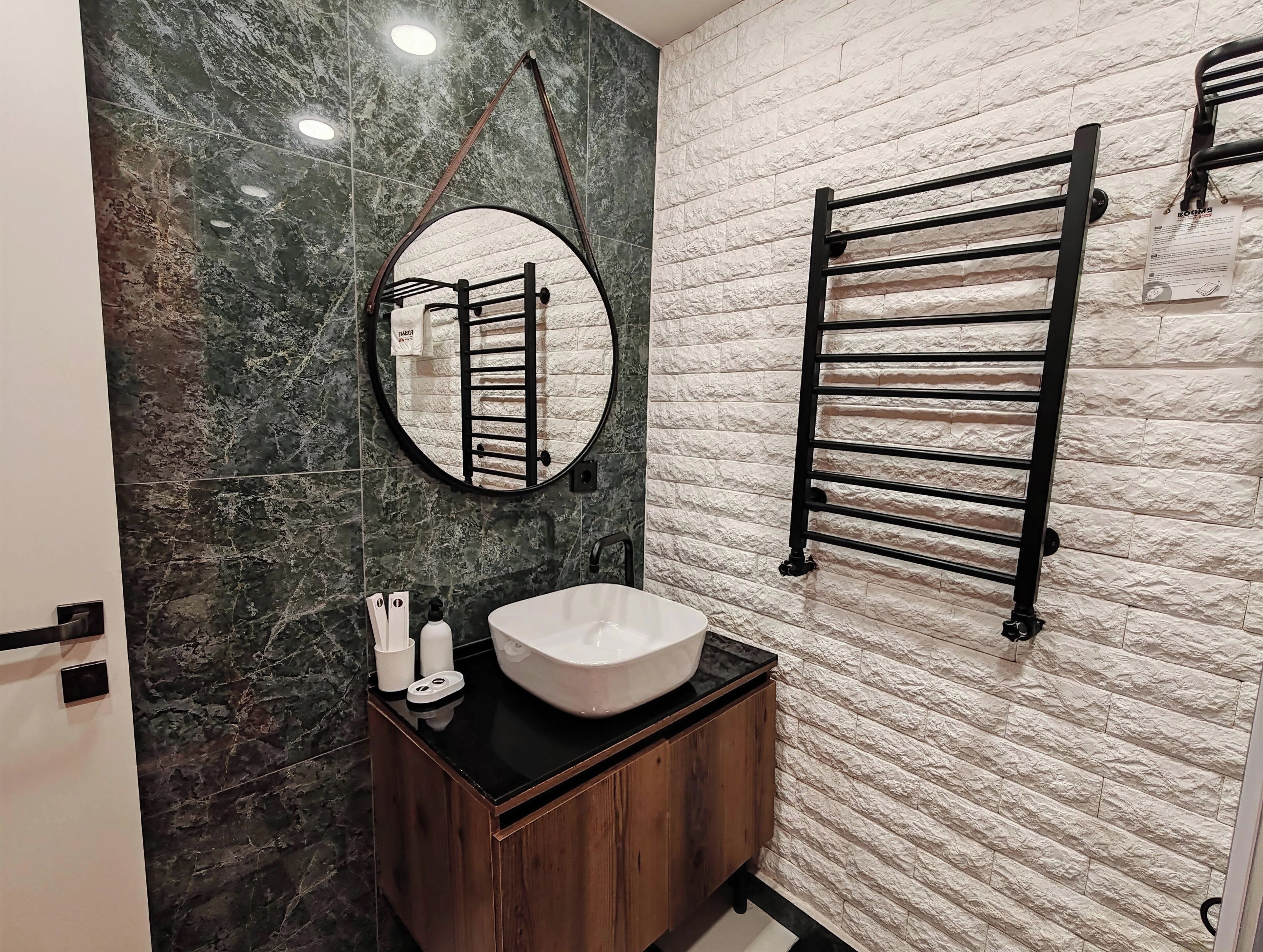 A bathroom with a round mirror, a towel rack, a sink, and a wooden cabinet.