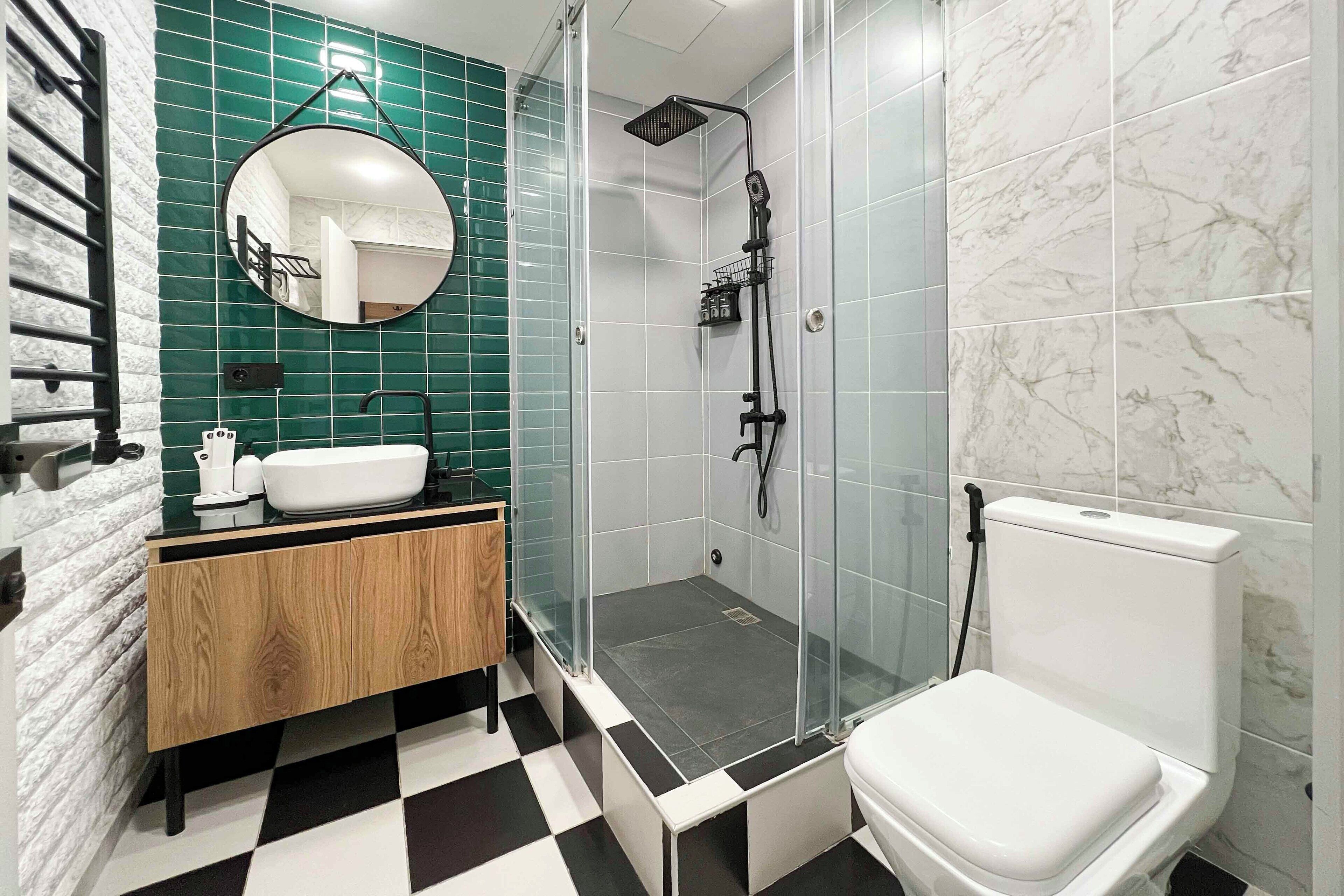 A modern bathroom with a checkered floor, a wooden vanity, a white sink, a round mirror, a glass-enclosed shower, and a toilet.