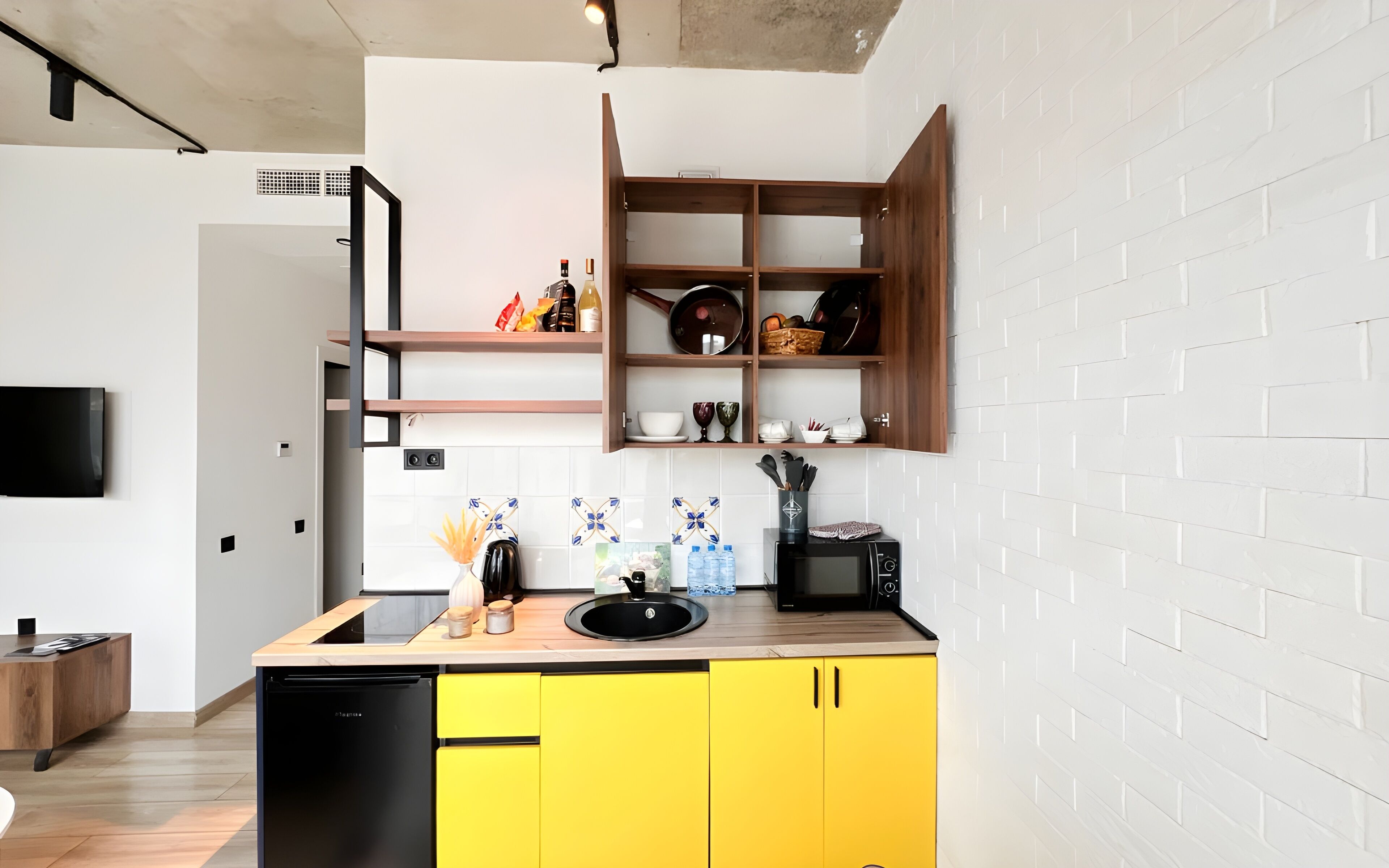 A modern kitchen with yellow cabinets, a black sink, and a wooden shelf unit above the countertop.
