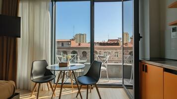 A modern room with a balcony, a dining table with chairs, a sofa, and a TV.