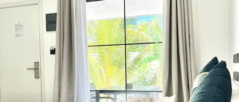 A hotel room with a bed, a window with curtains, a door, and an air conditioning unit.