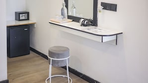Une salle de bain moderne avec un comptoir blanc, un miroir, un petit tabouret, un coffre-fort noir et un réfrigérateur compact.