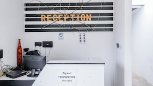 Un comptoir d’accueil avec une pancarte indiquant « RÉCEPTION » au-dessus, un ordinateur et un vase placés sur le côté gauche.