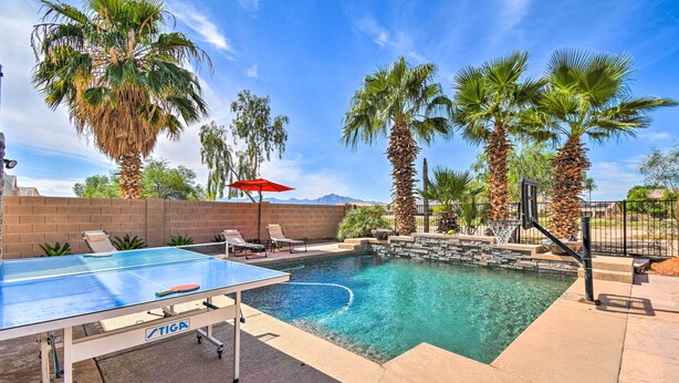 A swimming pool with a ping pong table, palm trees, and a red umbrella.
