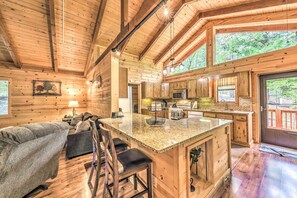 A log cabin interior with a kitchen, dining area, and a cozy seating area with a couch and chairs.