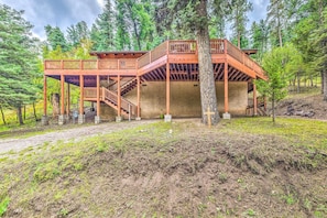 A wooden cabin with a balcony and stairs, surrounded by trees.
