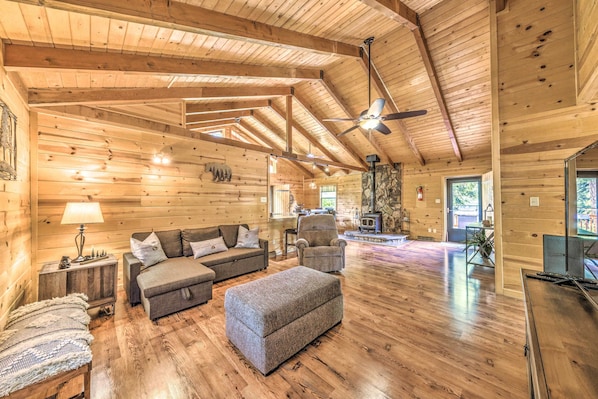 A spacious log cabin interior with a large living area, a fireplace, and a ceiling fan.
