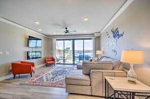 A spacious living room with a large window, a ceiling fan, and a flat-screen TV mounted on the wall.