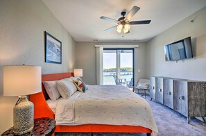 Une chambre d’hôtel avec un lit, un ventilateur de plafond, une télévision, une fenêtre donnant sur un beau paysage et un balcon.