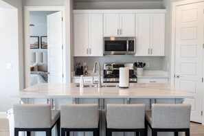 A modern kitchen with white cabinetry, a central island with bar stools, a stainless steel microwave, and a gas stove.