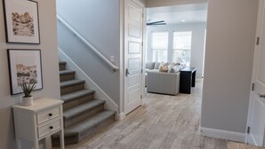 Un pasillo con una escalera, una puerta blanca y un sofá gris al fondo.