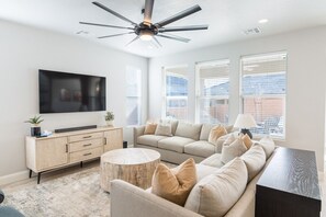 A modern living room with a sectional sofa, a round coffee table, a TV mounted on the wall, and a ceiling fan.