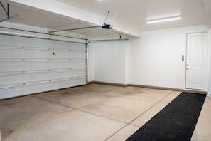 Un garage propre et vide, avec une porte de garage fermée, un tapis noir à l’entrée et un projecteur fixé au plafond.