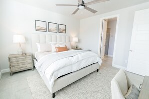 Une chambre à coucher avec un lit, des tables de chevet, un ventilateur de plafond et des tableaux encadrés accrochés au mur.