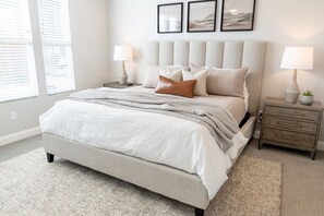 A bedroom with a bed, two bedside tables, a nightstand, and a window with blinds.