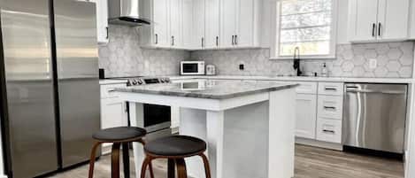 A modern kitchen with white cabinetry, stainless steel appliances, a central island, and a window providing natural light.