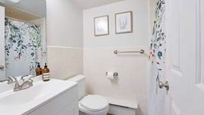 Ein Badezimmer mit einem weißen Waschbecken, einer Toilette und einer Dusche. An der Wand hängen zwei gerahmte Bilder und ein Duschvorhang mit Blumenmuster.