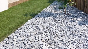 A landscaped garden with a wooden deck, a small tree, and a gravel path. - Charming Bas de villa beach walking natural site (Venzolasca)