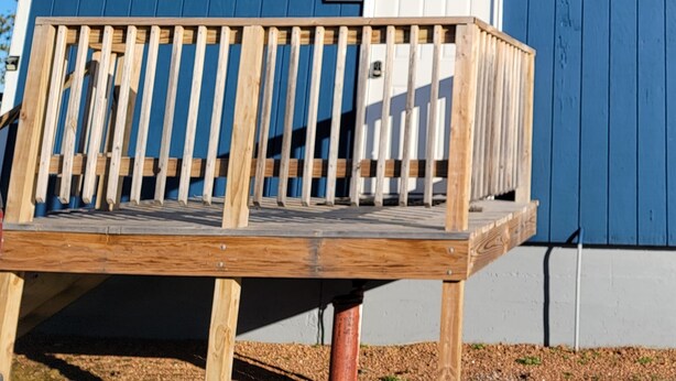 Una terraza de madera con una puerta blanca y un edificio azul al fondo.