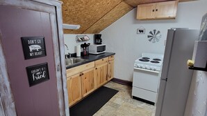 Una cocina con armarios de madera, una estufa blanca y un refrigerador. Hay letreros en la puerta y un microondas en la encimera.