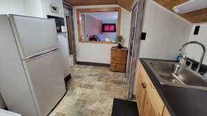 Una cocina compacta con nevera, armarios de madera, un lavabo y una ventana con cortinas.