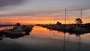 Een jachthaven in de zonsondergang, met aanmerende boten en kalm water dat de lucht weerspiegelt.