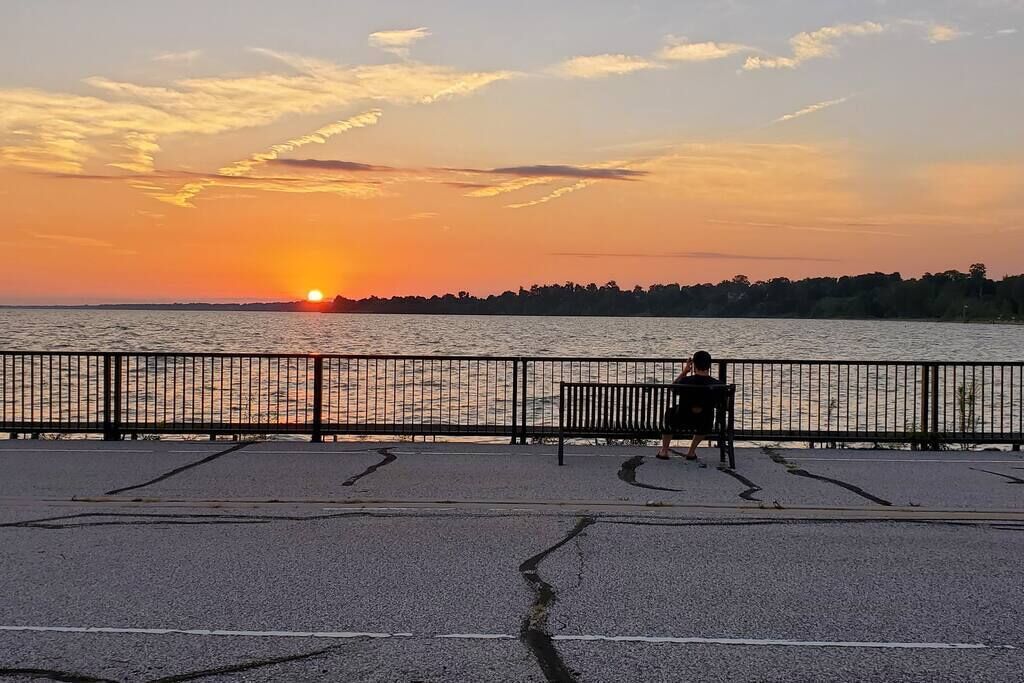 A sunset view from a waterfront promenade with a bench and a fence.