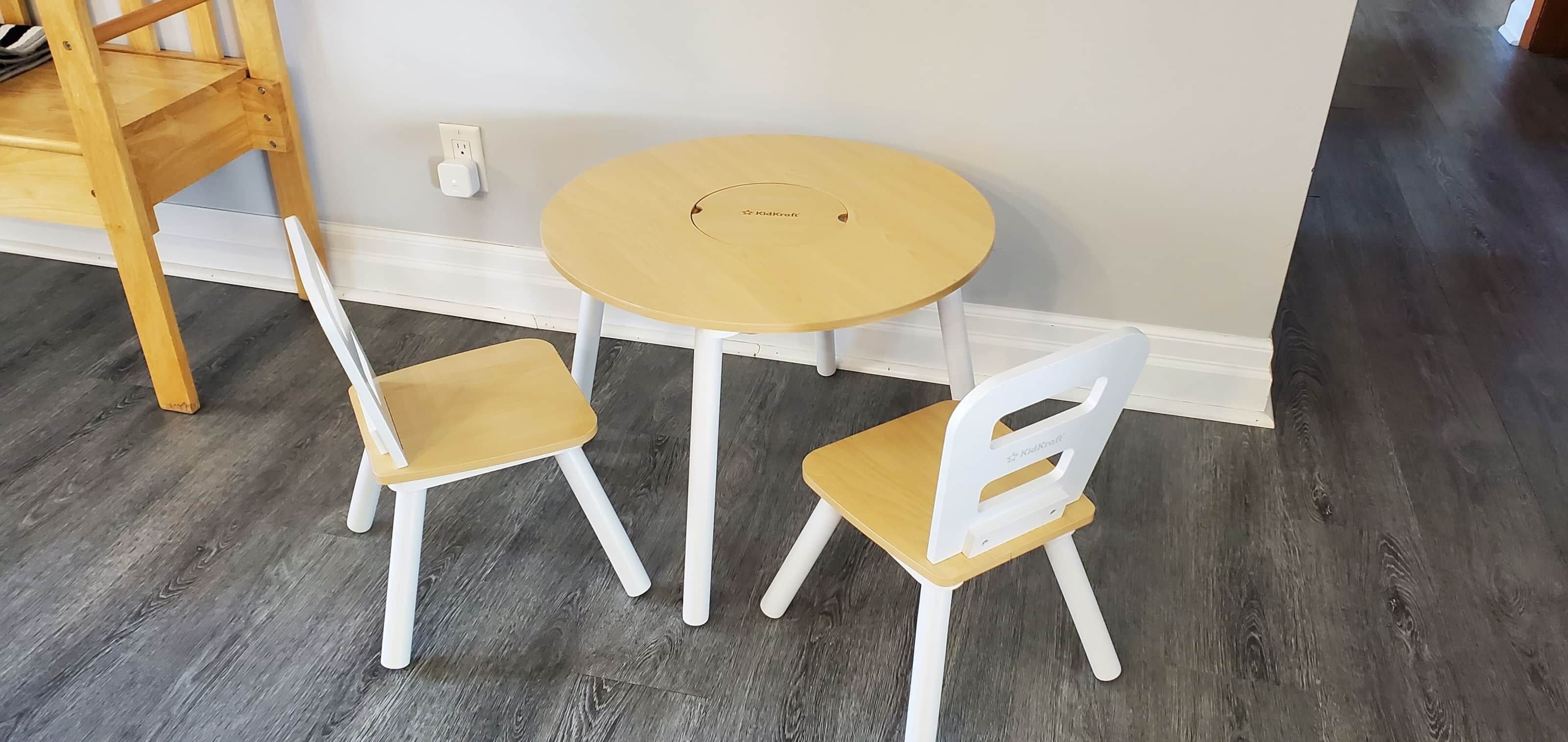 Una habitación pequeña con una mesa redonda de madera y dos sillas blancas.