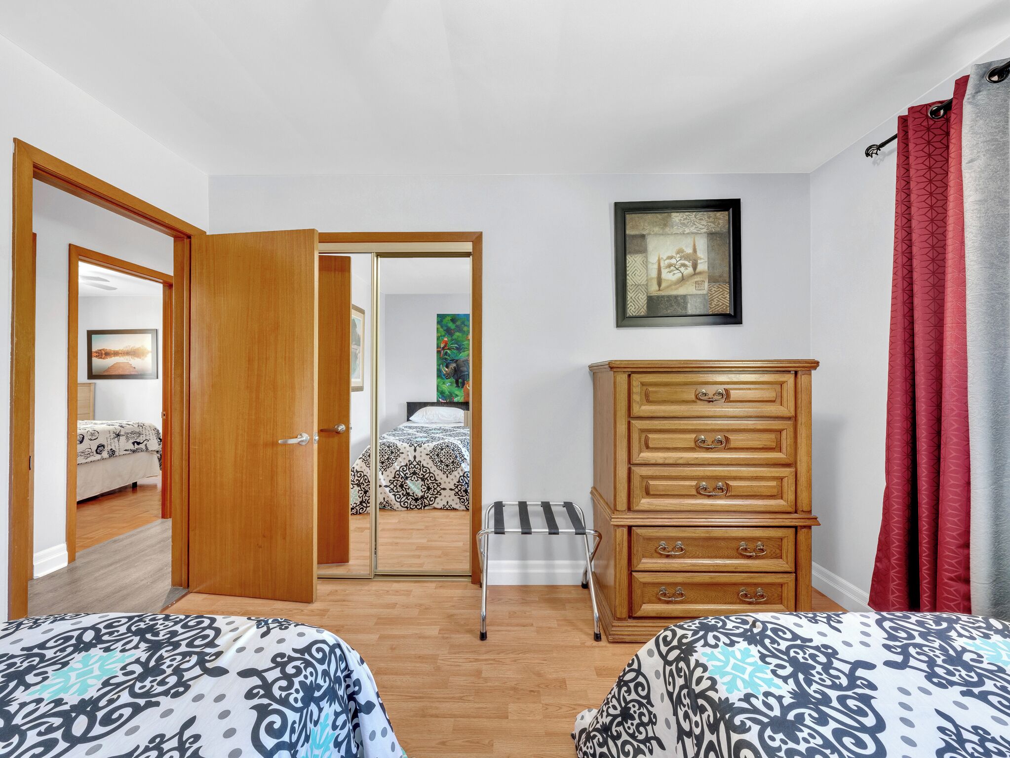 Un dormitorio con dos camas, un aparador de madera, un cuadro enmarcado en la pared y una cortina roja.