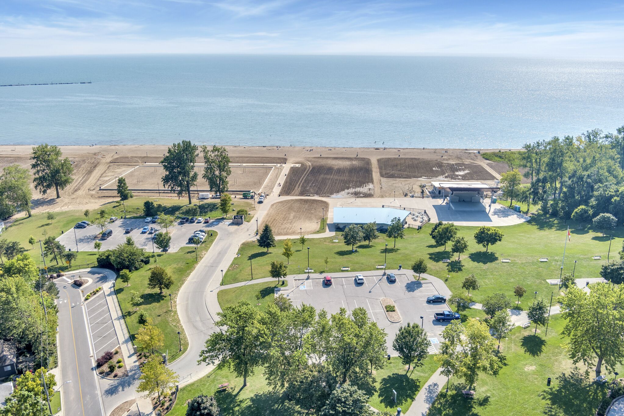 An aerial view of a coastal area with a parking lot, green spaces, and a large building with a blue roof.