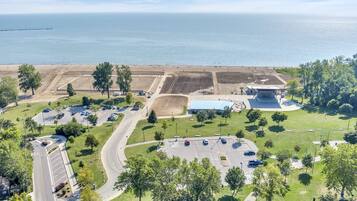 An aerial view of a coastal area with a parking lot, green spaces, and a large building with a blue roof.