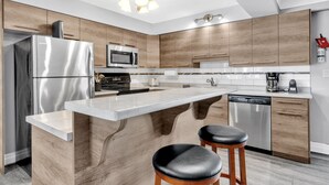 Een moderne keuken met een centraal eiland, roestvrijstalen apparatuur, houten kastjes en een geïntegreerde vaatwasser.
