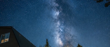 A house with a porch under a starry night sky, surrounded by trees.