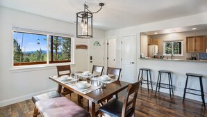 A dining area with a wooden table set for four, a bench, and a view of a forest through large windows. - NEW Updated, SUNSETCABIN:3 bd,1.5 bth, secluded, beautiful views, deck, sleeps 6 (Florissant)