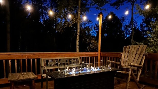 An outdoor deck with a built-in fire feature, wooden furniture, and string lights. - NEW Updated, SUNSETCABIN:3 bd,1.5 bth, secluded, beautiful views, deck, sleeps 6 (Florissant)