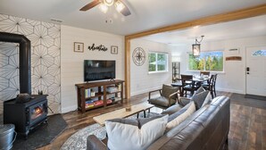 A spacious living room with a fireplace, a television, and a dining area with wooden furniture. - NEW Updated, SUNSETCABIN:3 bd,1.5 bth, secluded, beautiful views, deck, sleeps 6 (Florissant)