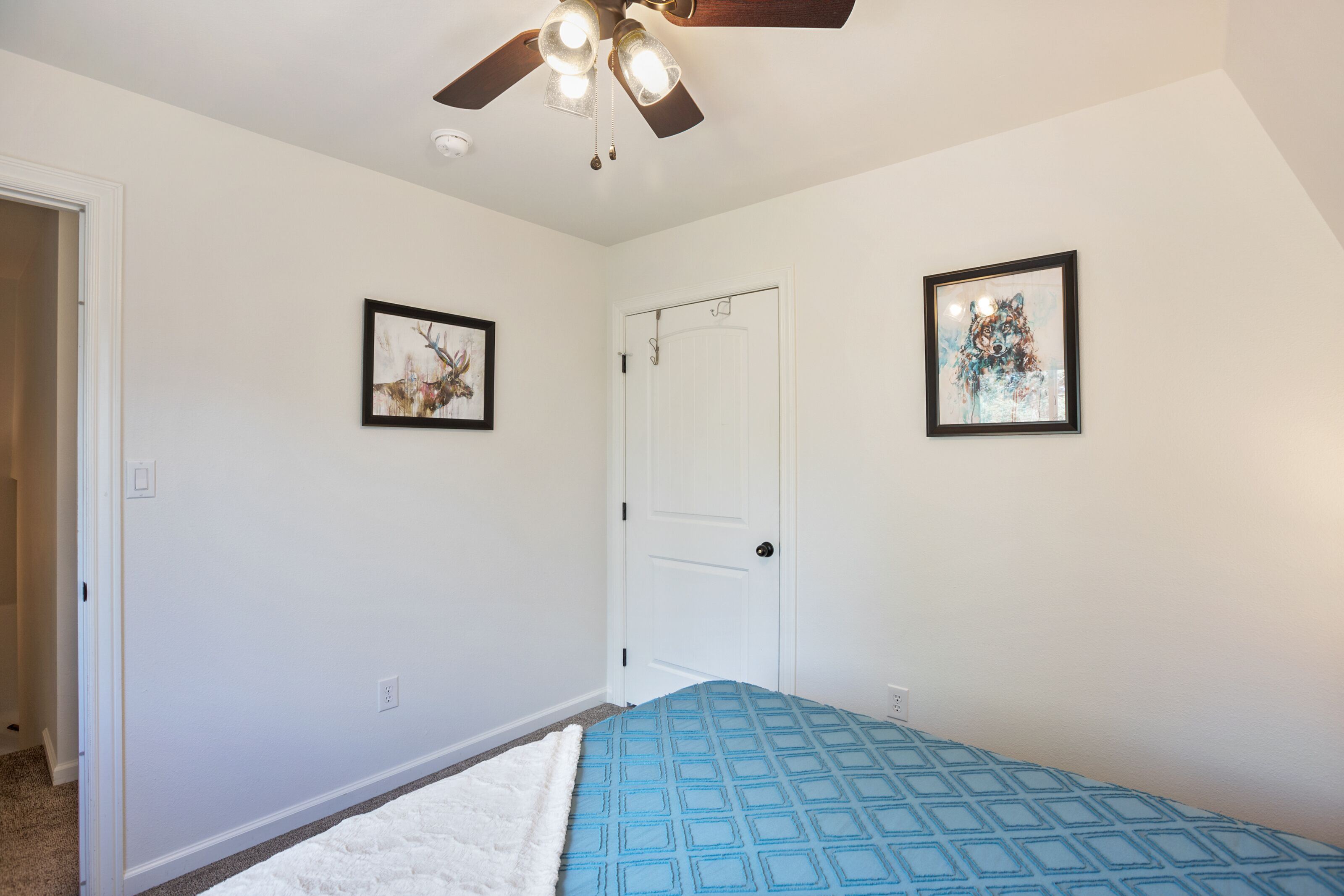 Une chambre à coucher avec un lit, un ventilateur de plafond et deux tableaux encadrés accrochés aux murs.