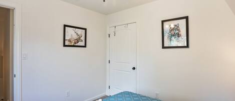 Une chambre à coucher avec un lit, un ventilateur de plafond et deux tableaux encadrés accrochés aux murs.