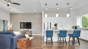 A modern kitchen with white cabinets, stainless steel appliances, and blue bar stools.