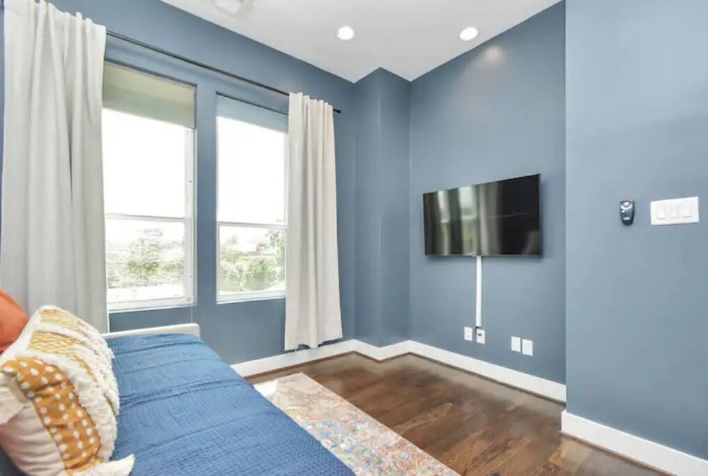 Une chambre avec un lit, un téléviseur fixé au mur et une fenêtre avec des rideaux.