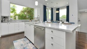 A modern kitchen with white cabinetry, a large island, and a view of greenery outside.