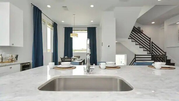A modern kitchen with a central island, stainless steel sink, and a staircase leading to an upper level.