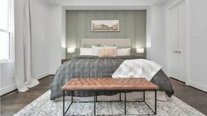A bedroom with a large bed, a bench, a wall-mounted painting, and a door.