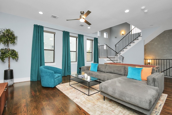 A modern living room with a gray sofa, teal curtains, and a glass coffee table.