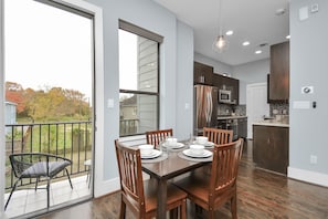 A modern kitchen with stainless steel appliances, a dining area with wooden chairs and a table set for four, and a sliding glass door leading to a balcony.