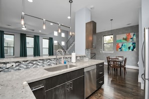 A modern kitchen with a large island, stainless steel appliances, and a dining area with wooden chairs.