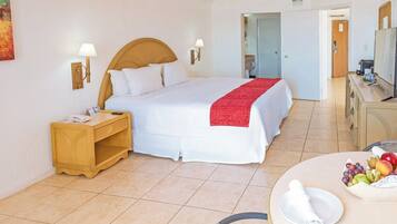 Habitación de hotel con una cama grande, mesitas de noche, un escritorio y un área de comedor con fruta.