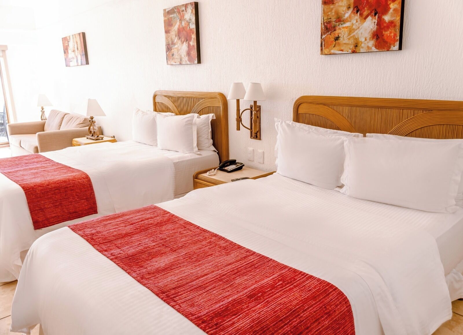 Een hotelkamer met twee bedden, elk voorzien van witte lakens en rode plaids. Er zijn wandlampen, nachtkastjes met een telefoon en kunstwerken aan de wanden.