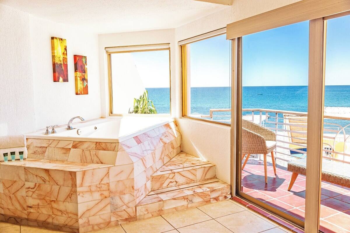 Un baño con lavamanos de mármol, bañera y un amplio ventanal con vistas al mar.